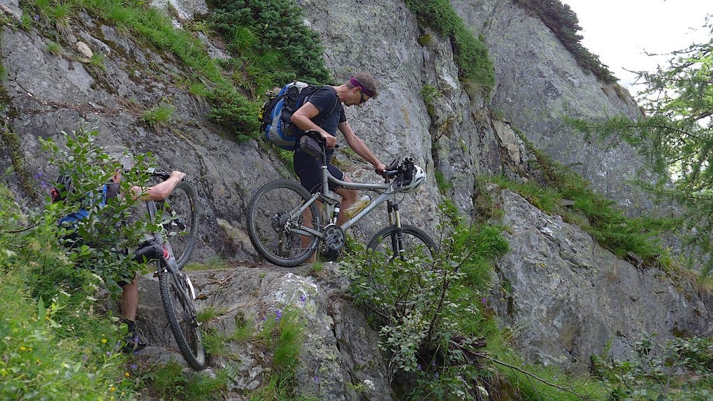 Mountainbiker schieben beim Schweizcross durch eine Felswand