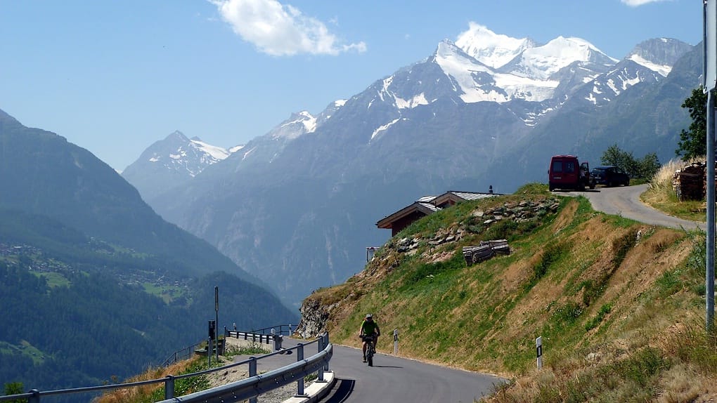 Mit den Walliser Bergen im Hintergrund fährt ein Mountainbiker eine Straße hoch
