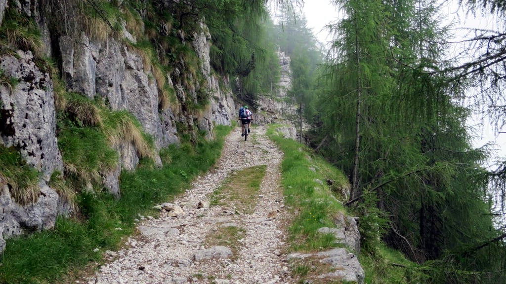 ein Mountainbiker fährt eine alte Militärstraße hoch. Links die Wand, rechts der Abgrund